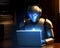 Robot works with laptop at table in dark room background with gadgets in light.Training of robots and artificial