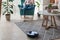 Robotic vacuum cleaner cleaning carpet, woman controls remote control and joy rest while sitting on armchair home