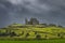 Rock of Cashel castle on green hill illuminated by sunlight with storm clouds in background