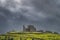 Rock of Cashel castle illuminated by sunlight and surrounded by dramatic dark storm clouds