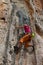 Rock climber girl in orange pants leaging climbing route on natural rock