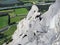 Rock climber on a steep and exposed limestone climbing crag in the Swiss Alps above lush green fields below