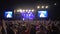 Rock festival, many people enjoy and clap on live music concert against brightly lit stage with large screens at night