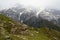 Rock formations and green meadows against snow covered ranges