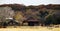 Rock house and Barn with round hay bales backed up to Autumn trees on hill with cows in pens in front - Beautiful scene