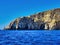 Rock islands on blue sea. Summer desk space. Breaking wave over a small rock on a sea shore. Rio`s mountain with a cave in the