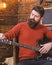 Rock musician with brutal look posing with instrument. Bearded man tuning electric guitar. Man with stylish beard and