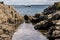 A rock pool with water and a ship on the sea.