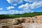 Rock quarry with hills above covered in forest and meadows