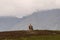 Rock shrine topped with cross high in mountains with higher misty mountains in background