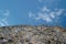 Rock or stone on blue sky with clouds background. Granite crouan rim or pick edge like cliff or mountain. Geology mineral texture