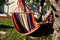 Rocking chair, hammock with wooden support among the trees in the garden. view of naked hairy white legs of a rocking man, striped