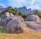 Rocks and boulders against a majestic mountain background with lush green trees and a clear blue sky. Remote and quiet