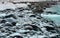 Rocks covered in snow flakes on the banks of a turquoise and white river