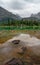 Rocks and logs in the clear alpine water of Lake O`Hara high in the Canadian Rockies with cabins and mountains in the overcast bac