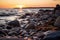 rocks and pebbles on the shore of a body of water at sunset