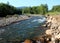 The rocky bank of a small turbulent river flowing down from the mountains through the coniferous forest