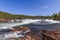 Rocky banks and cascades of Namsen River with dense forest on sunny day in Trondelag, Norway