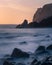 A rocky California coastline with birds sitting on the rocks watching the sunset with smooth waves in the foreground