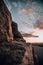 a rocky cliff at sunset with the sun setting on the ocean in the distance