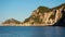 Rocky cliffs with some trees at Liapades bay lit by morning sun, calm sea water and boat buoys in foreground