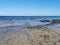 The rocky coast of the Mediterranean Sea from long-hardened lava, waves, clear water against a blue sky with clouds