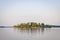 Rocky island overgrown with birch forest on a calm mountain lake in the rays