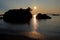 Rocky islet and reefs silhouetted against the late evening sun which glints off of the calm sea