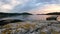 Rocky land beach with vibrating sea water and cliffs on the horizon under sunset sky