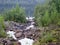 A rocky landscape with trees and rocks in the foreground. Suna River, Poor Porog Waterfall, Girvas