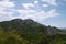 The rocky mountain peak against the background of a bright sky with transparent clouds overgrown on the slopes by a rare