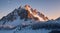 A rocky mountain peak with snow, catching the last light of the day