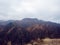 Rocky mountain ranges with dry yellow grass, bare autumn trees and overhanging clouds.