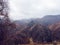 Rocky mountains with dry yellow grass, bare autumn trees and overhanging clouds.