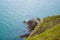 Rocky outcrop at the base of cliffs in Wicklow, Ireland on sunny day in summer. Green hillslide and turquoise-blue Irish Sea