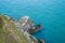 Rocky outcrop at the base of cliffs in Wicklow, Ireland on sunny day in summer. Green hillslide and turquoise-blue Irish Sea