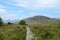 A rocky path, in the center of the image, leads across grassland meadow to mountains in Snowdonia