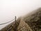 Rocky path with chain fence surrounded by thick mist on high mountains