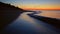Rocky seashore at orange sunset dawn. Peaceful seascape at dark sand beach