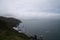 Rocky seawall with mountains and hills with ocean and clouds to right