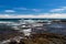 Rocky shoreline, Black Sand Beach, Hawaii. Rocks, blue ocean and waves; blue sky, clouds in background.