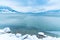 Rocky shoreline, calm blue water, and mountains in distance with storm clouds