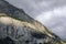 Rocky slope of alpine mountain with grey cloudy sky. Alpine landscape with scanty vegetation. Switzerland.