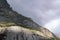 Rocky slope of alpine mountain with grey cloudy sky. Alpine landscape with scanty vegetation. Switzerland.