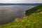 Rocky steep forested and grassy shore of the river bay in cloudy weather. Panoramic view of the river in summer in cloudy weather