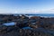 Rocky volcanic shoreline in Hawaii. Low tide; pools of water in rock cavities. Waves, ocean blue sky and clouds in background.
