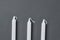 Roe of three long candles on dark concrete