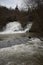 Roes, Germany - 02 09 2021: wild Elz waterfall under the medieval bridge during snow melting season, the lake and lower cascades