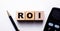 ROI Return on investment written on wooden cubes between calculator and pen on light background. Investment concept