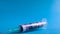 A roll of 100 dollars money inserted into a white medical hypodermic needle on a blue background. The concept of health care costs